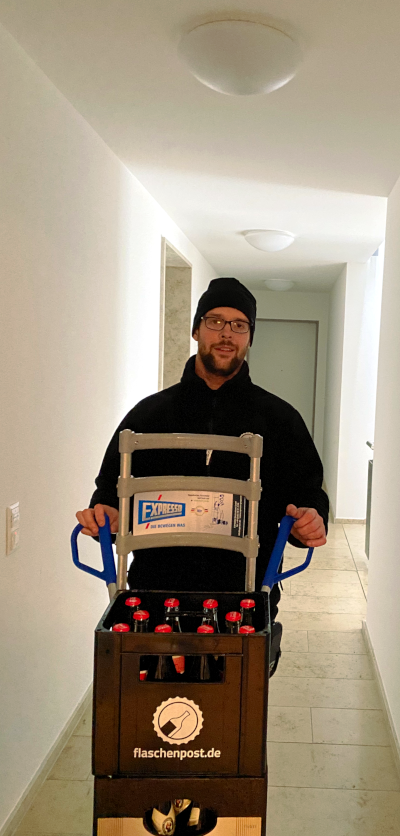 Der freundliche Lieferant mit seiner Sackkarre, der Cola Kasten zeigt an seiner Front das Flaschenpost Logo