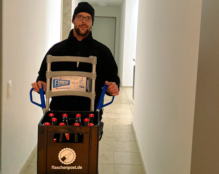 Der freundliche Lieferant mit seiner Sackkarre, der Cola Kasten zeigt an seiner Front das Flaschenpost Logo